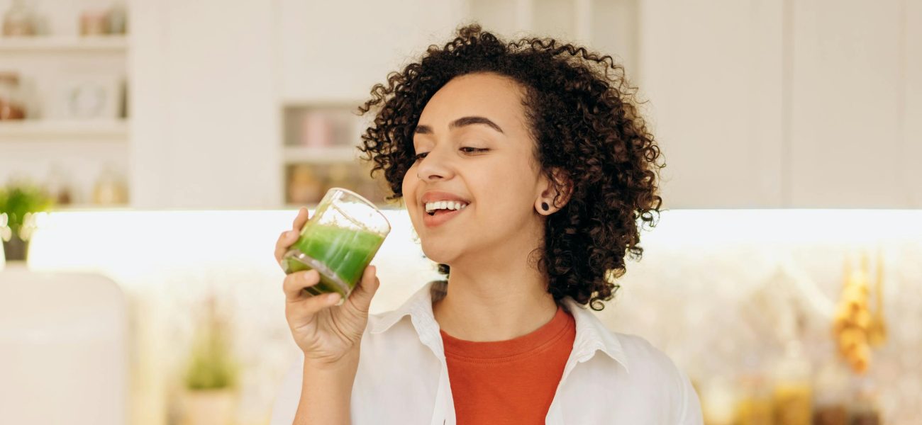 A woman in a kitchen drinking a green smoothie