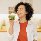 A woman in a kitchen drinking a green smoothie