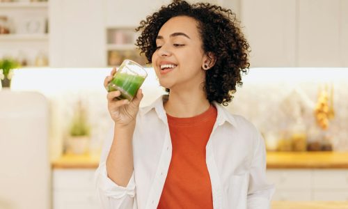 A woman in a kitchen drinking a green smoothie