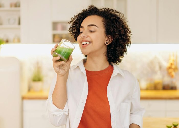 A woman in a kitchen drinking a green smoothie