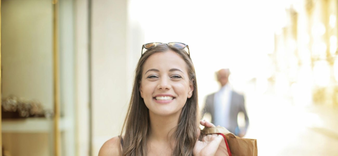A smiling woman holding shopping bags over her shoulder on a summer day