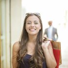 A smiling woman holding shopping bags over her shoulder on a summer day