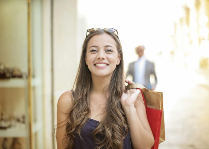 A smiling woman holding shopping bags over her shoulder on a summer day