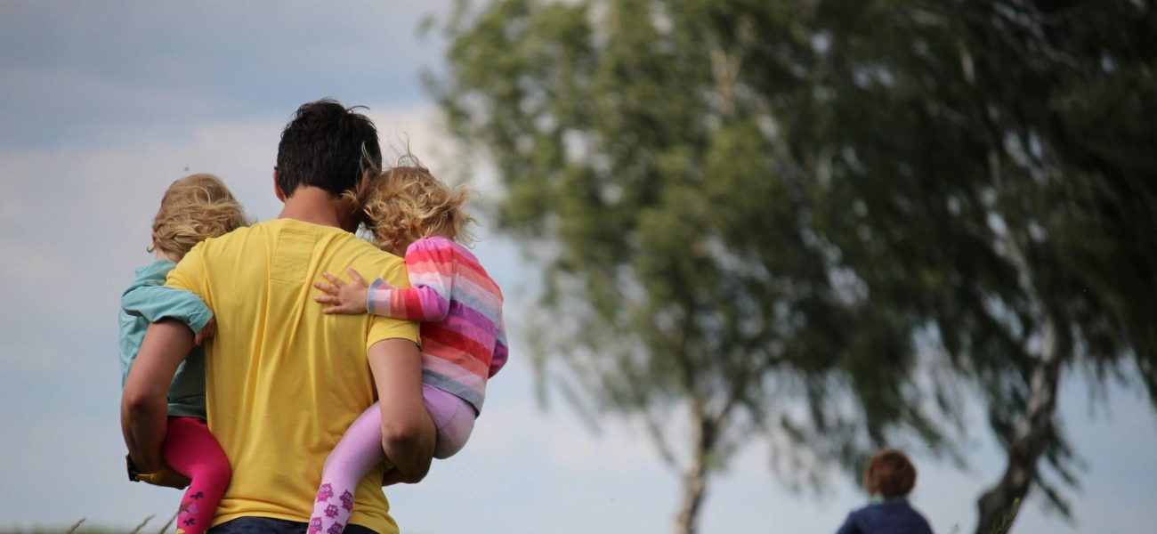 A father carrying two children through a field
