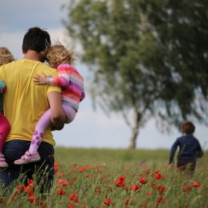 A father carrying two children through a field