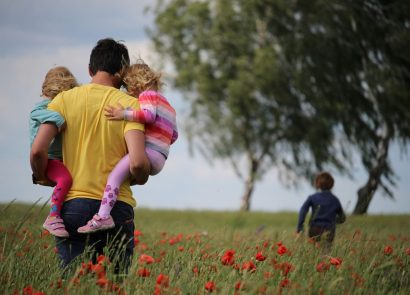 A father carrying two children through a field