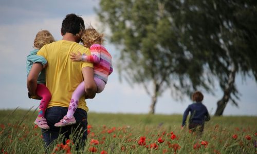 A father carrying two children through a field
