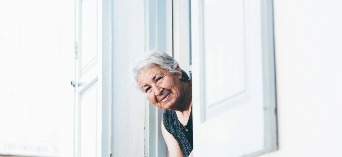 An elderly woman leaning out of an upstairs window of her home