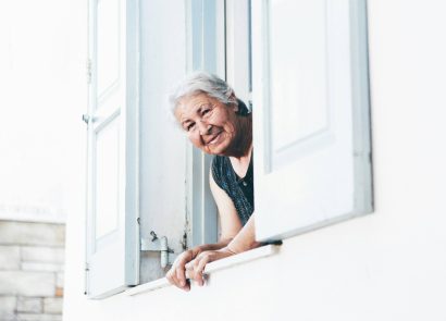 An elderly woman leaning out of an upstairs window of her home