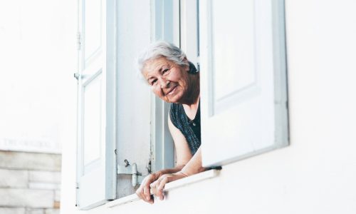An elderly woman leaning out of an upstairs window of her home