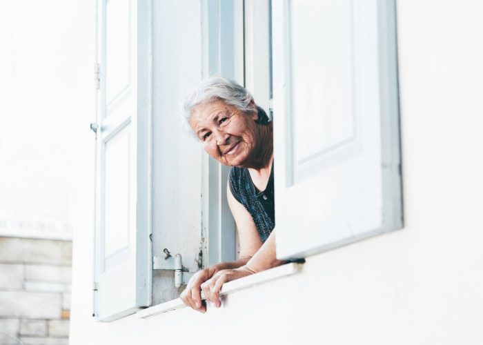 An elderly woman leaning out of an upstairs window of her home