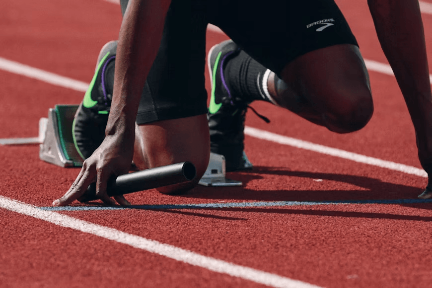 An athlete in the starting blocks on a running track holding a baton