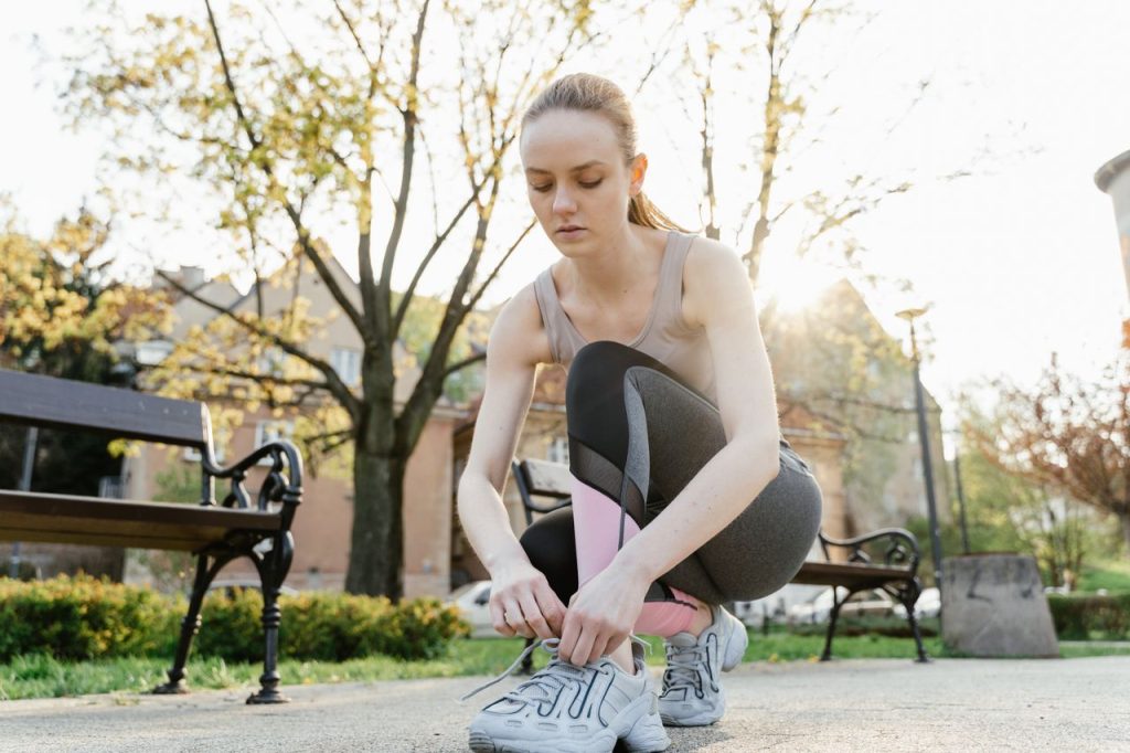 A woman in fitness wear crouching on a pavement to tie her shoe