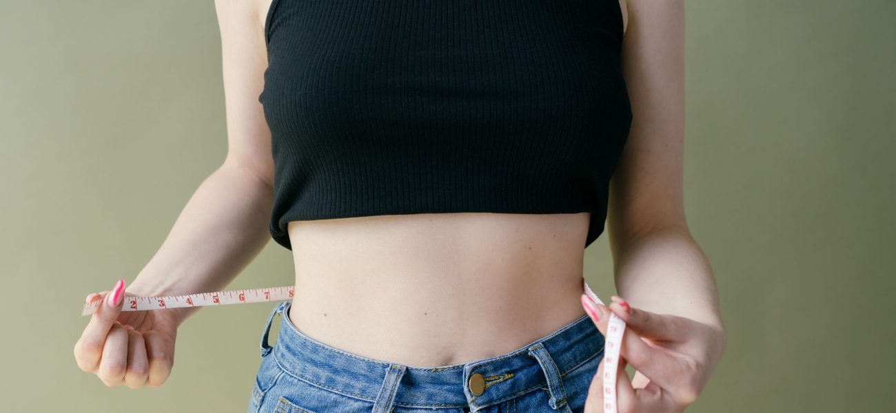 A woman wearing jeans holding a measuring tape around her waist