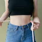 A woman wearing jeans holding a measuring tape around her waist
