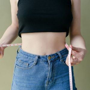 A woman wearing jeans holding a measuring tape around her waist