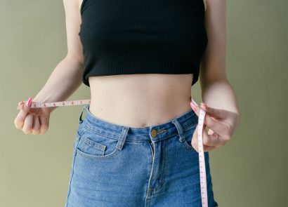 A woman wearing jeans holding a measuring tape around her waist