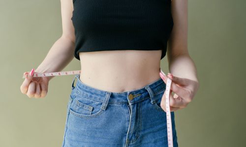 A woman wearing jeans holding a measuring tape around her waist