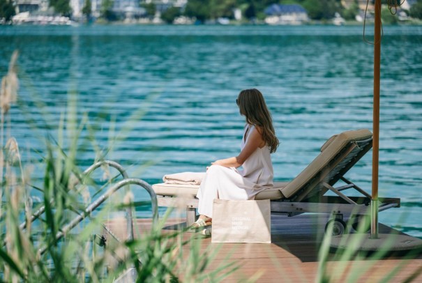 A woman sitting on a sun lounger by the water at the Original Mayr Medical Resort