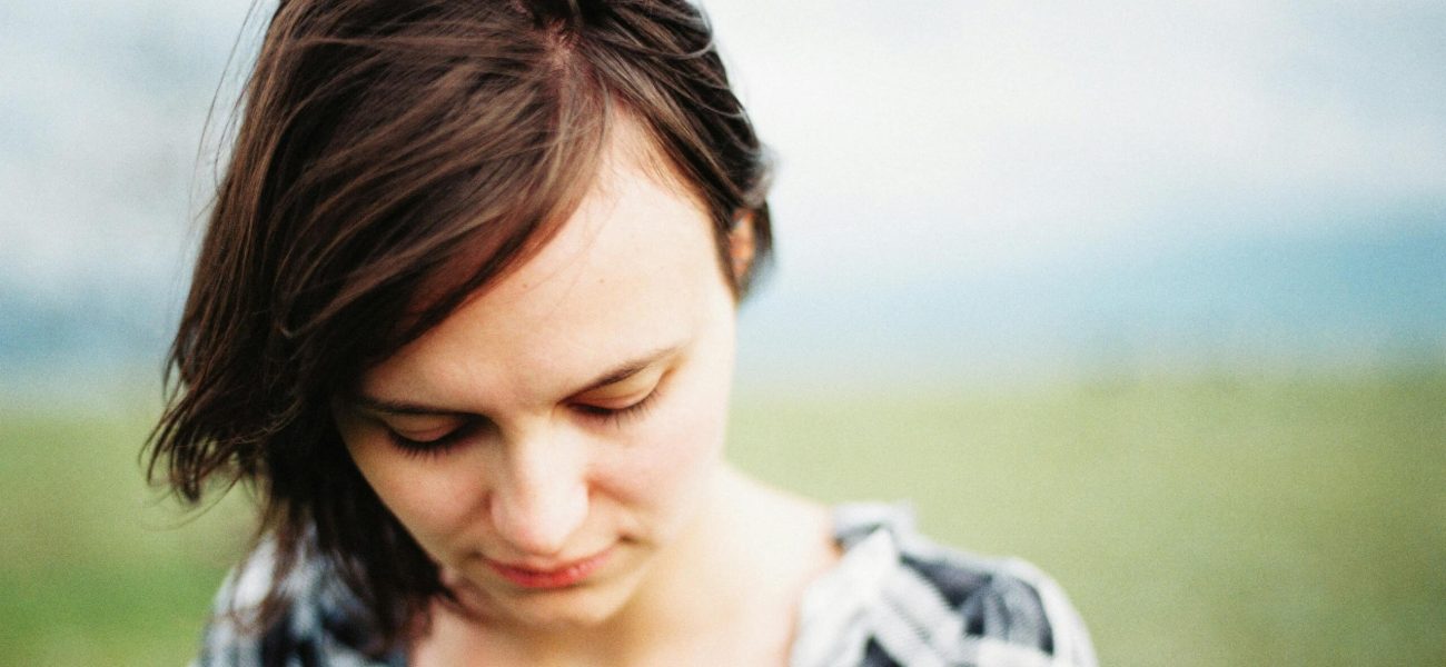 A woman with brown hair walking outside, looking down towards the ground