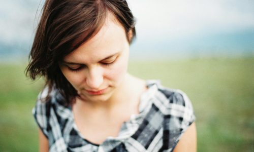 A woman with brown hair walking outside, looking down towards the ground