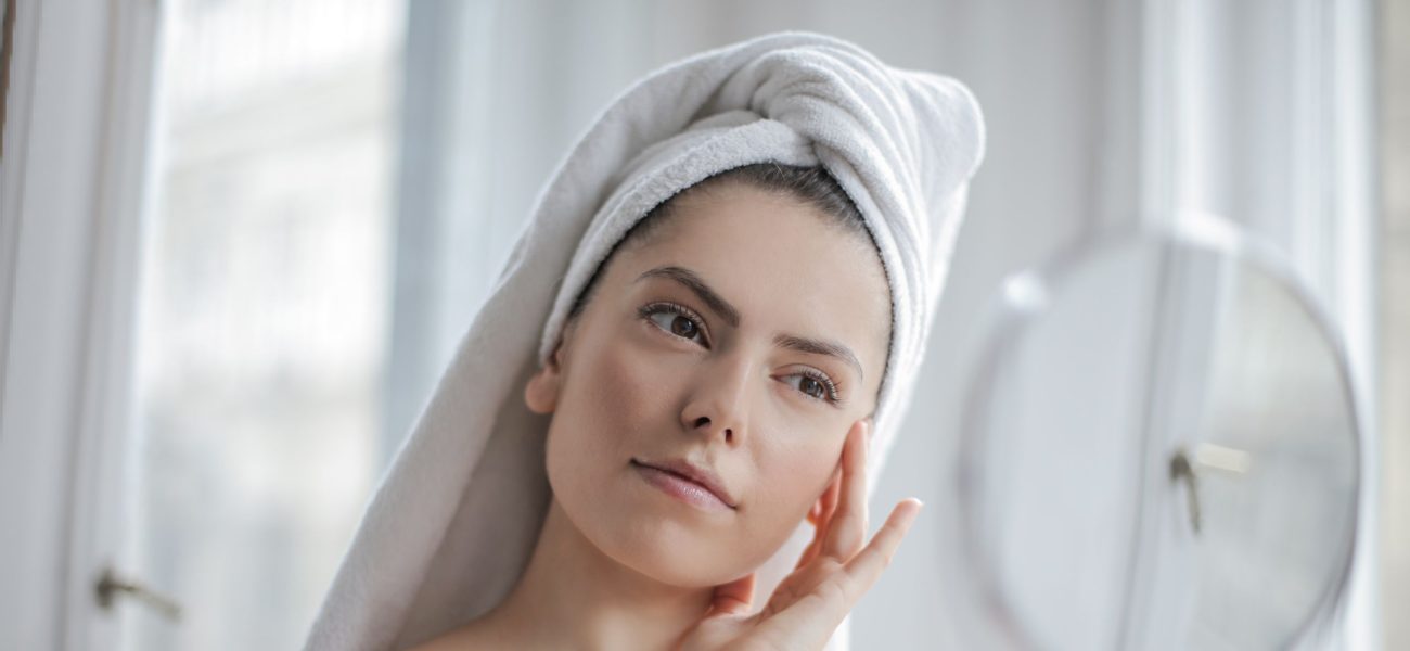 A woman in her bathroom looking into a mirror as part of her skincare routine
