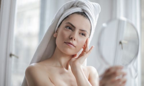 A woman in her bathroom looking into a mirror as part of her skincare routine