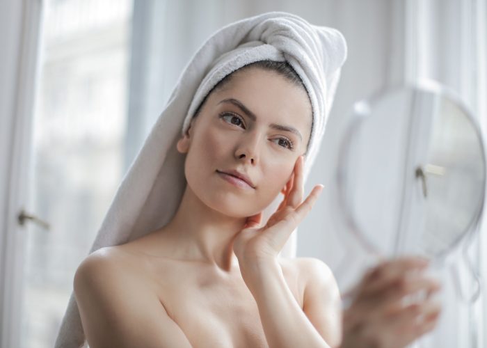 A woman in her bathroom looking into a mirror as part of her skincare routine