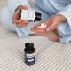A woman tipping Hypnozan capsules into her hand as she sits on a bed; another jar of Hynozan is beside her on the duvet