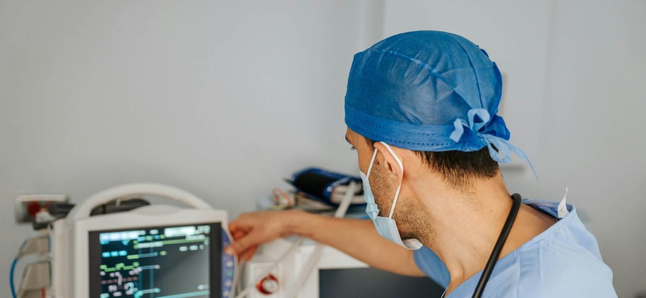 A doctor in surgical scrubs in front of a medical monitoring screen