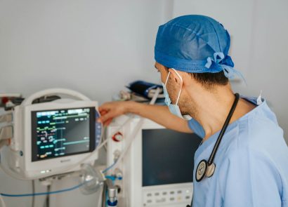A doctor in surgical scrubs in front of a medical monitoring screen