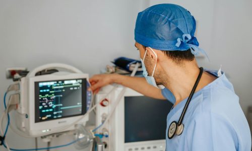 A doctor in surgical scrubs in front of a medical monitoring screen