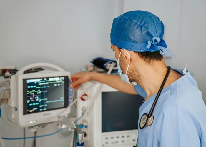 A doctor in surgical scrubs in front of a medical monitoring screen