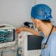A doctor in surgical scrubs in front of a medical monitoring screen