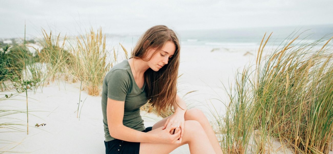 A woman sitting on a sandy beach holding her knee