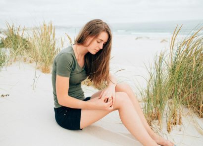 A woman sitting on a sandy beach holding her knee