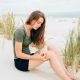 A woman sitting on a sandy beach holding her knee