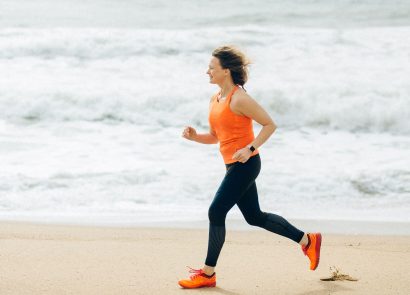 A middle-aged woman jogging on a beach with the sea behind her