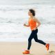 A middle-aged woman jogging on a beach with the sea behind her