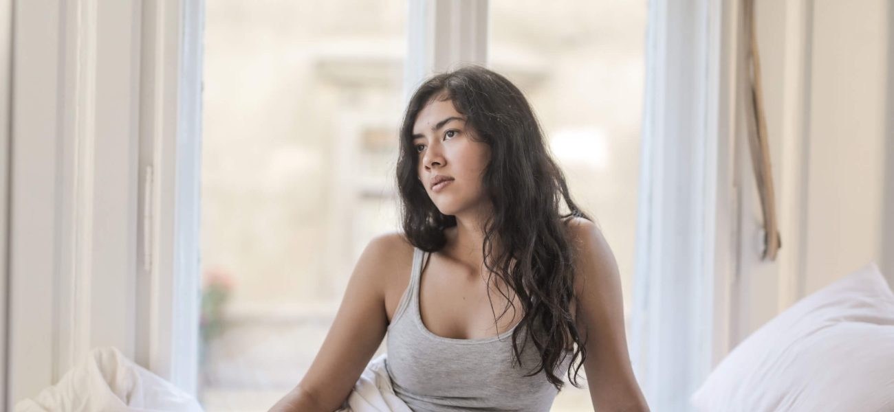 A young dark-haired woman sitting on a bed in front of a window