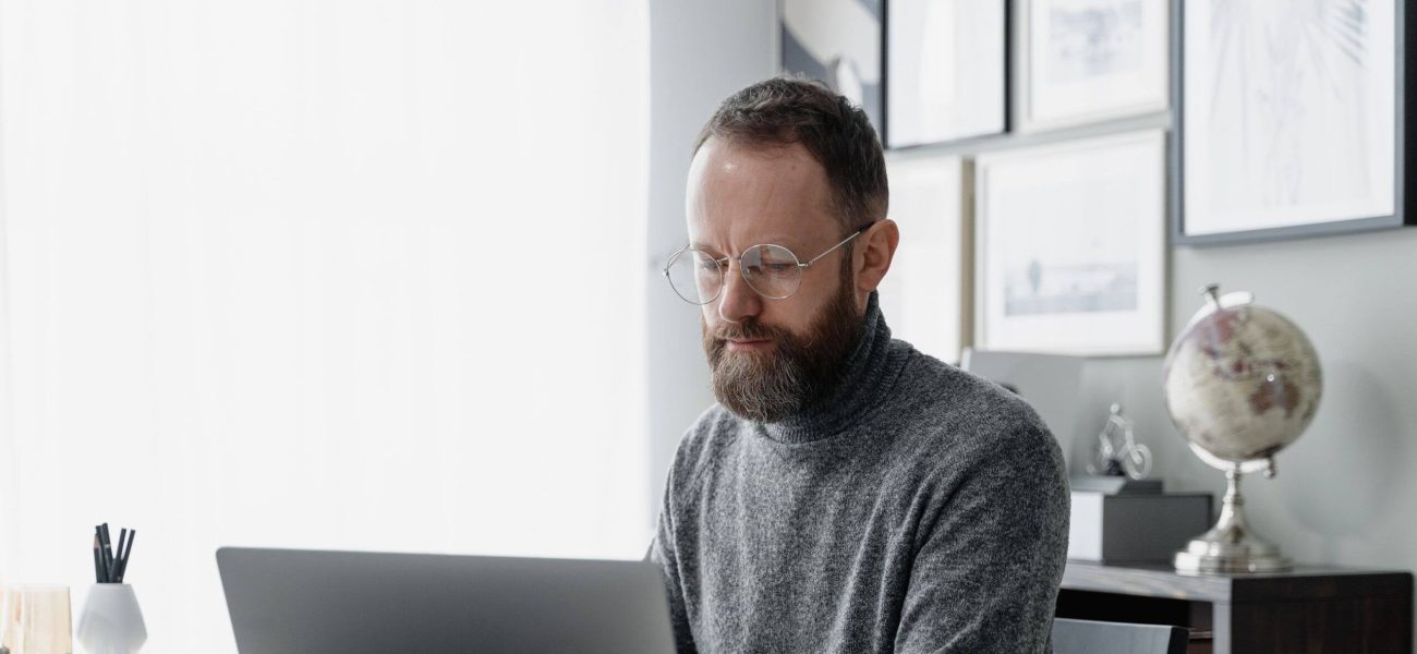 A man with glasses sitting at a desk using a laptop computer