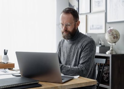 A man with glasses sitting at a desk using a laptop computer