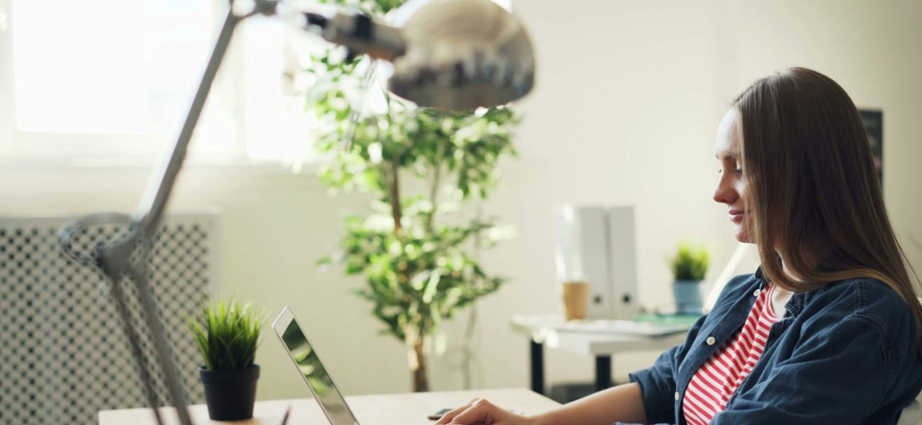 A side-on shot of a woman sitting at a desk typing on a laptop computer