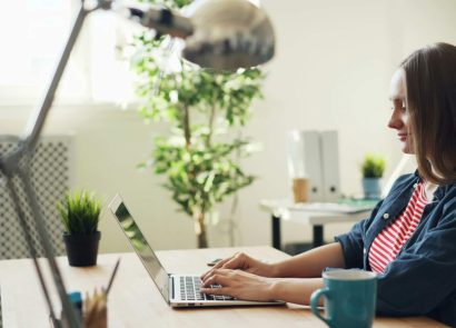 A side-on shot of a woman sitting at a desk typing on a laptop computer