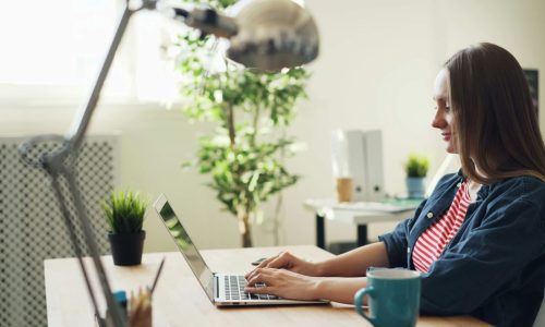 A side-on shot of a woman sitting at a desk typing on a laptop computer
