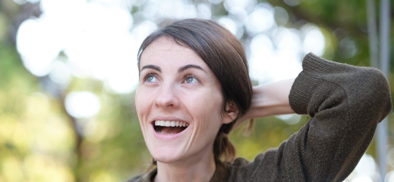 A smiling woman holding her hair outdoors