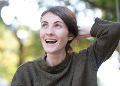 A smiling woman holding her hair outdoors