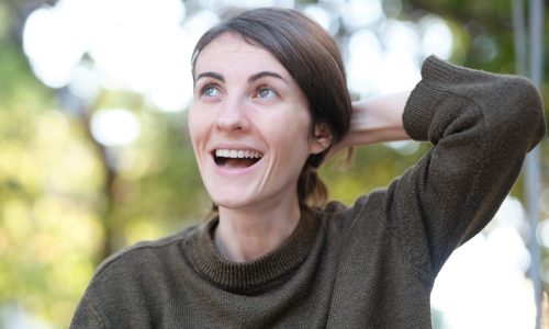 A smiling woman holding her hair outdoors