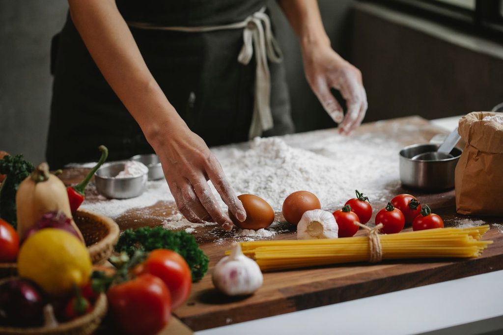 A chef preparing a dish consisting of eggs, spaghetti, tomatoes and flour in a home kitchen