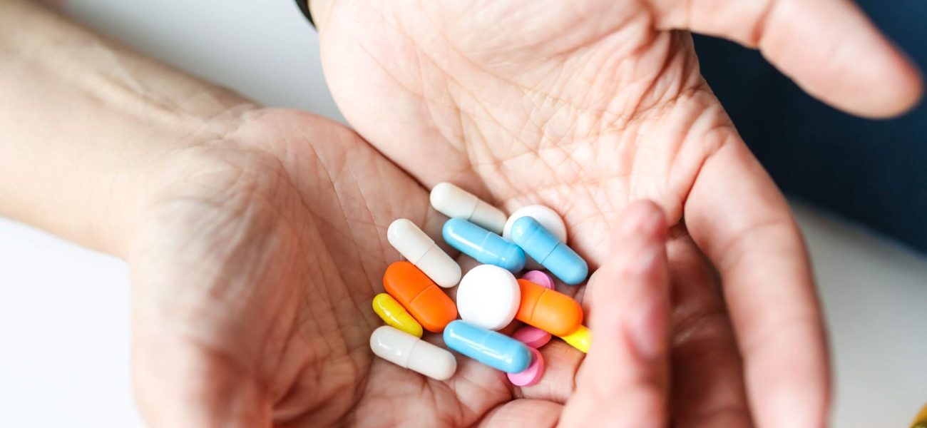 A woman's hands holding a variety of tablets and capsules